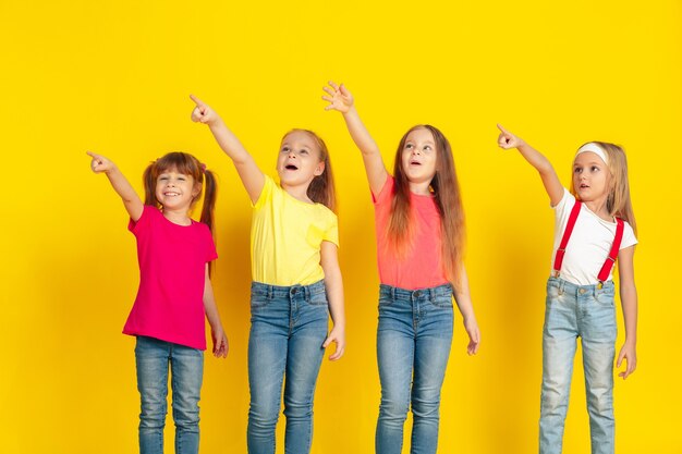 Indicazione. Bambini felici che giocano e si divertono insieme su sfondo giallo studio. I bambini caucasici in abiti luminosi sembrano giocosi, ridenti, sorridenti. Concetto di educazione, infanzia, emozioni.