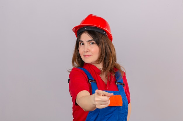 Indossare l'uniforme della costruzione della donna del costruttore e indicare del casco di sicurezza dispiaciuto e frustrato la macchina fotografica sopra isolata mentre parete