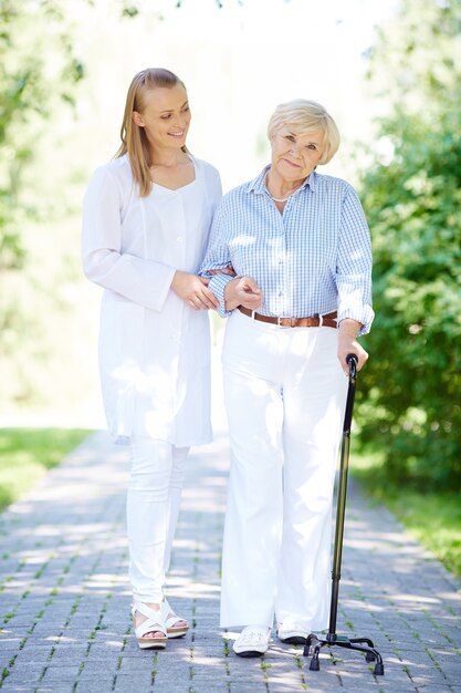 Infermiera che aiuta donna maggiore con bastone da passeggio