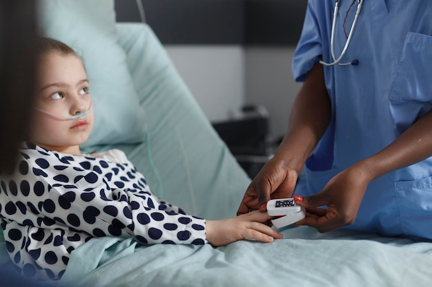 Infermiera che misura i livelli di ossigeno della bambina malata ricoverata che riposa sul letto del paziente. Bambino malato seduto nel reparto pediatrico dell'ospedale mentre il personale medico monitora le condizioni di salute usando l'ossimetro.