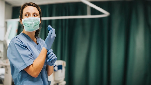 Infermiera con una maschera che indossa i guanti che si prepara a curare il paziente con coronavirus