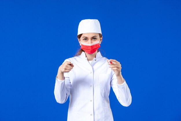 Infermiera femminile di vista frontale in vestito medico bianco con maschera rossa e iniezione nelle sue mani sull'azzurro