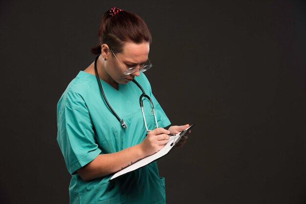 Infermiera femminile in uniforme verde che tiene il vuoto e scrive la storia.