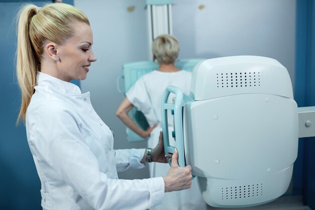 Infermiera sorridente della metà degli adulti che prende i raggi X di un paziente alla clinica