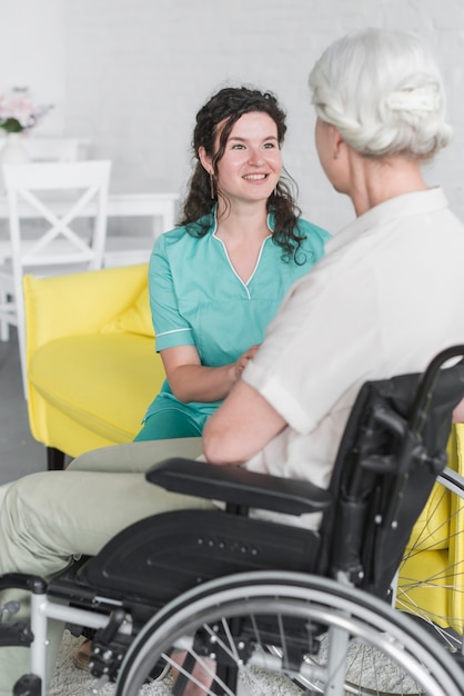 Infermiere sorridente che sostiene donna senior disabile che si siede sulla sedia a rotelle