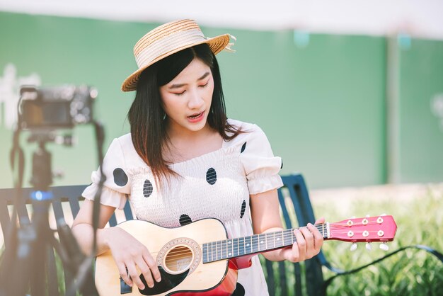 Influencer donna asiatica che suona la chitarra nel parco per creare uno stile di vita contenuto e un concetto di ricreazione