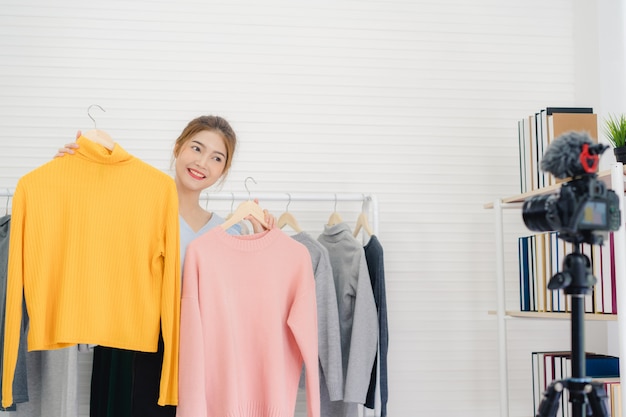 Influencer online di blogger femminile della moda asiatica che tiene i sacchetti della spesa e molti vestiti