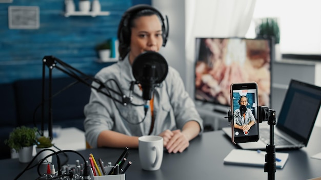 Influencer sui social media che utilizza un laptop moderno durante lo streaming di podcast a distanza sullo smartphone. Creatore di contenuti digitali creativi che registra vlog giornalieri con un moderno dispositivo cellulare touchscreen.