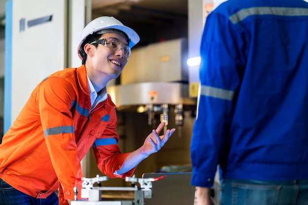 Ingegnere asiatico maschio professionista che ha una discussione in piedi concult macchina cnc nella fabbrica due colleghi asiatici brainstorming spiegando e risolvendo il processo della macchina cnc opera