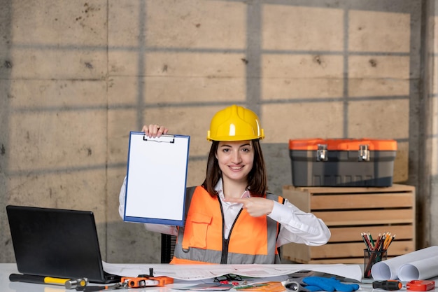 Ingegnere carino giovane ragazza bruna intelligente lavoratore civile in casco e giubbotto con progetto