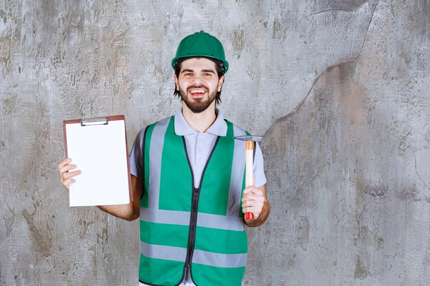 Ingegnere con equipaggiamento giallo e casco che tiene in mano un'ascia con manico in legno e una tasklist