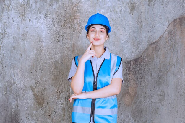 Ingegnere donna che indossa casco blu e attrezzatura e pensa o pianifica.