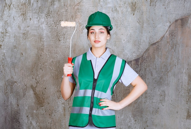 Ingegnere donna in casco verde che tiene un rullo di rifinitura per la pittura murale