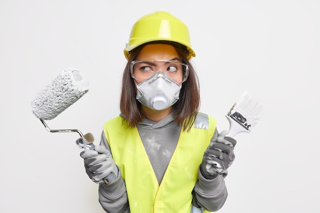 Ingegnere edile femminile in giubbotto di sicurezza occhiali protettivi maschera e guanti elmetto tiene l'attrezzatura sembra seriamente da parte pronta per entrare nell'area dell'edificio per l'ispezione. Operaio industriale.