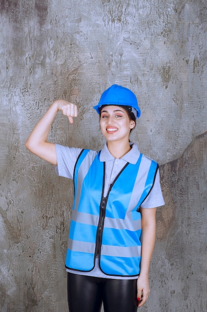 Ingegnere femminile che indossa casco e attrezzatura blu e mostra i muscoli del braccio.