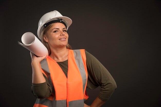 Ingegnere femminile con un casco bianco che tiene il piano di progetto e sembra positivo.