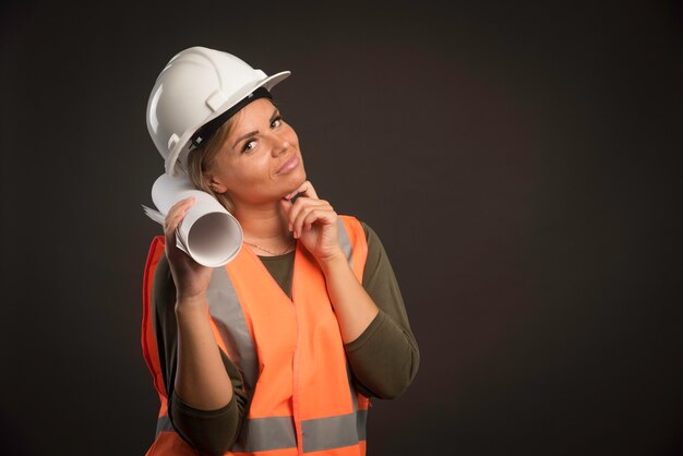 Ingegnere femminile con un casco bianco che tiene il piano di progetto.