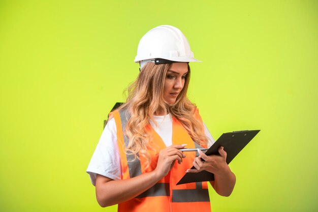 Ingegnere femminile in casco bianco e attrezzi che tengono la lista di controllo e che guardano al rapporto.