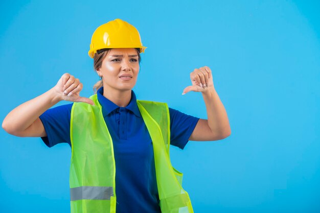 Ingegnere femminile in casco giallo e attrezzi che fanno i pollici giù.