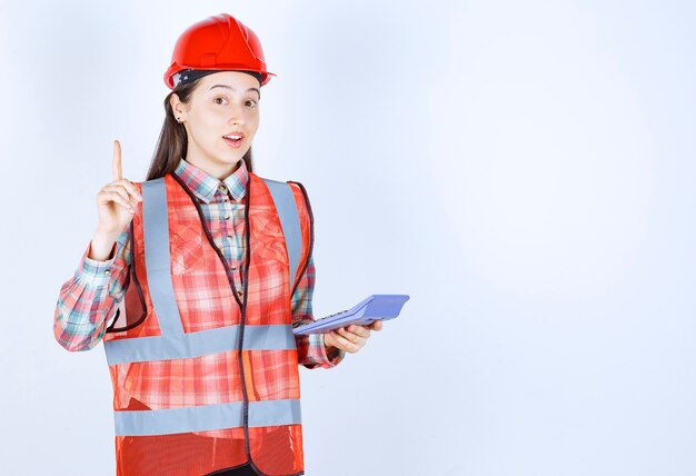 Ingegnere femminile in casco rosso che lavora alla calcolatrice e che ha un'idea.