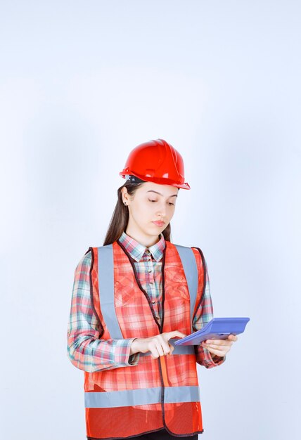 Ingegnere femminile in casco rosso che lavora alla calcolatrice.