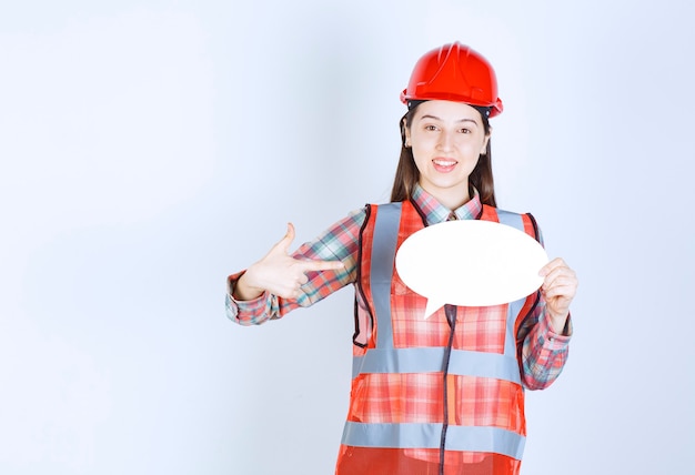 Ingegnere femminile in casco rosso che tiene una scheda info vuota.