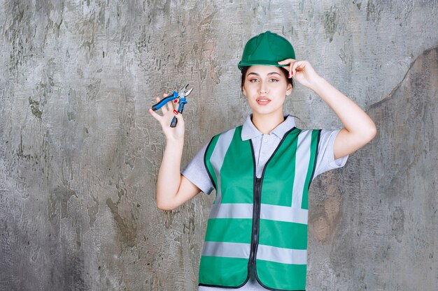 Ingegnere femminile in casco verde che tiene le pinze per un lavoro di riparazione.