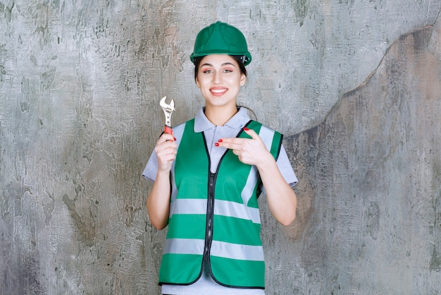 Ingegnere femminile in casco verde che tiene una chiave metallica per un lavoro di riparazione.