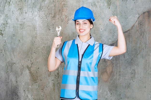 Ingegnere femminile in uniforme blu e casco che tiene una chiave metallica e che mostra il segno positivo della mano.