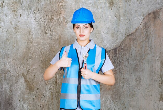 Ingegnere femminile in uniforme blu e casco che tiene una chiave metallica.