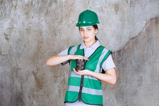 Ingegnere femminile in uniforme verde e casco che tiene una tazza di caffè nero.