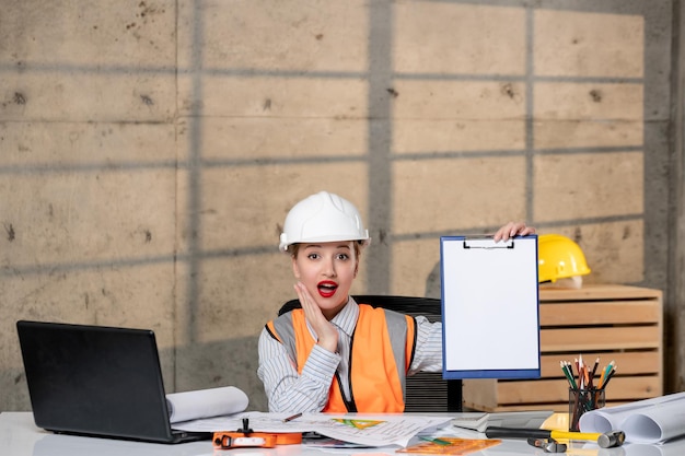 Ingegnere giovane ragazza bionda intelligente intelligente lavoratore civile in casco e gilet chiamando dipendente