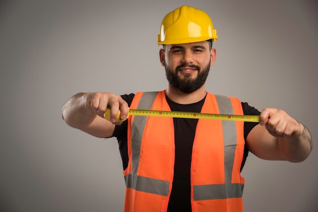 Ingegnere in uniforme arancione e casco giallo con righello