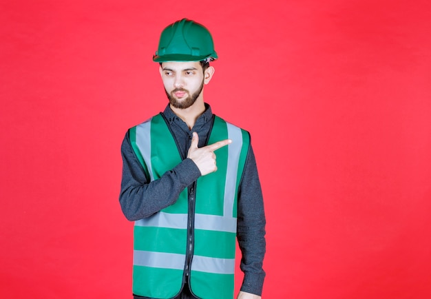 Ingegnere in uniforme verde e casco che indica la parte posteriore.