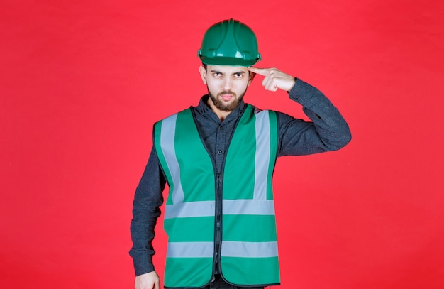 Ingegnere in uniforme verde e casco che pensa e pianifica.