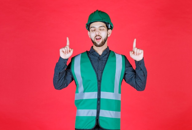 Ingegnere in uniforme verde e casco che punta sopra.