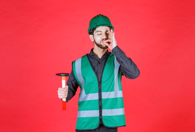 Ingegnere in uniforme verde e casco che tiene un'ascia di legno e mostra un segno positivo con la mano.