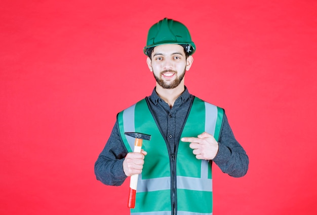 Ingegnere in uniforme verde e casco che tiene un'ascia di legno.