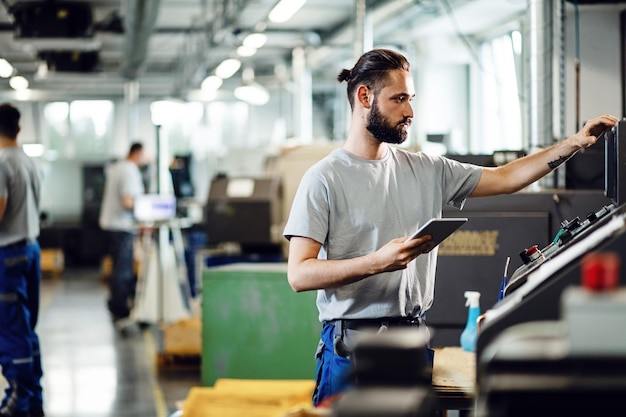 Ingegnere industriale che utilizza il touchpad durante il funzionamento di una macchina CNC in una fabbrica