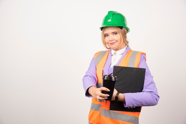 Ingegnere industriale della donna sorridente in uniforme con la lavagna per appunti e la tazza nera su bianco.