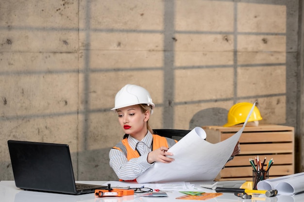 Ingegnere intelligente giovane ragazza bionda carina lavoratore civile in casco e giubbotto guardando il progetto