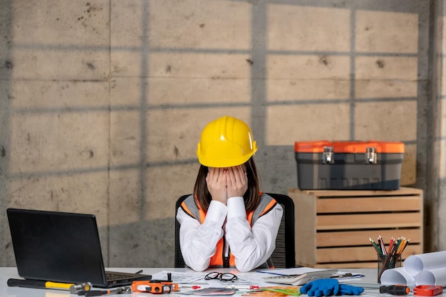 Ingegnere lavoratore civile in casco e gilet intelligente giovane ragazza bruna carina che copre il viso