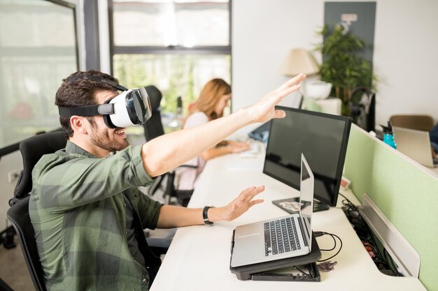 Ingegnere maschio che utilizza occhiali per realtà virtuale in ufficio con un collega in background