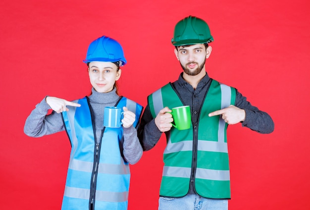 Ingegneri maschi e femmine con casco che tiene tazze blu e verdi.