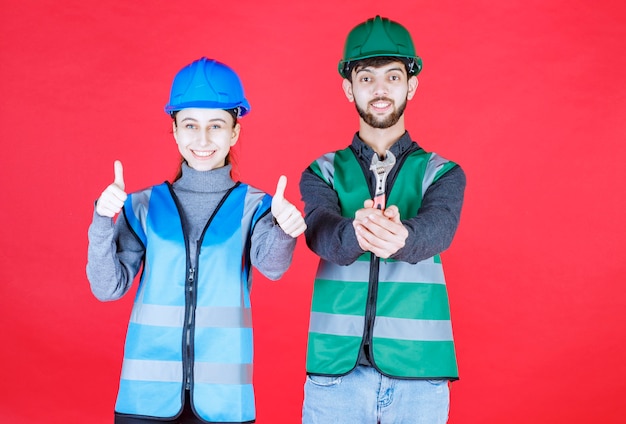 Ingegneri maschii e femminili con il casco che tiene una chiave metallica e che mostra il segno positivo della mano.