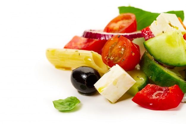 Ingredienti appetitosi colorati gustosi per insalata di verdure greca con penne di pasta su sfondo luminoso.