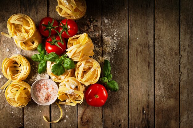 Ingredienti colorati freschi e saporiti per la cottura di pasta tagliatelle con basilico fresco e pomodori. Vista dall&#39;alto. Sfondo di tavola in legno.