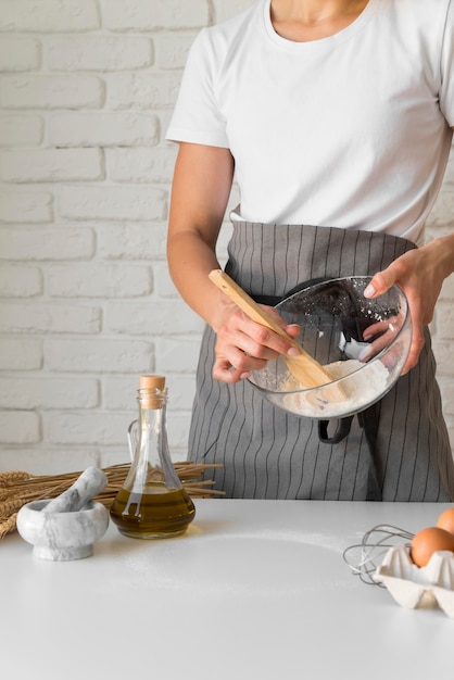 Ingredienti di miscelazione della donna in ciotola con il cucchiaio di legno