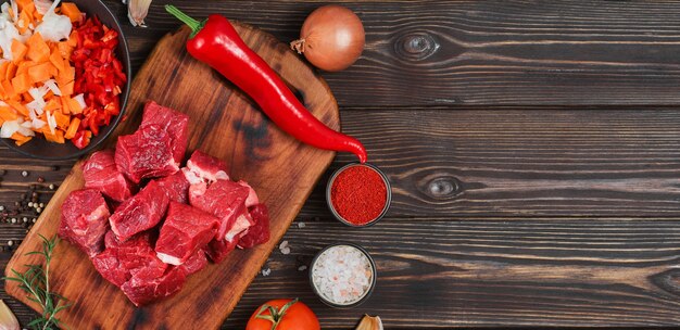 Ingredienti per preparare gulasch o spezzatino, spezzatino o gyuvech. vista dall'alto di carne di manzo cruda, erbe aromatiche, spezie, paprika, verdure sul tavolo di legno nero