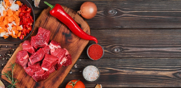 Ingredienti per preparare gulasch o spezzatino, spezzatino o gyuvech. vista dall'alto di carne di manzo cruda, erbe aromatiche, spezie, paprika, verdure sul tavolo di legno nero